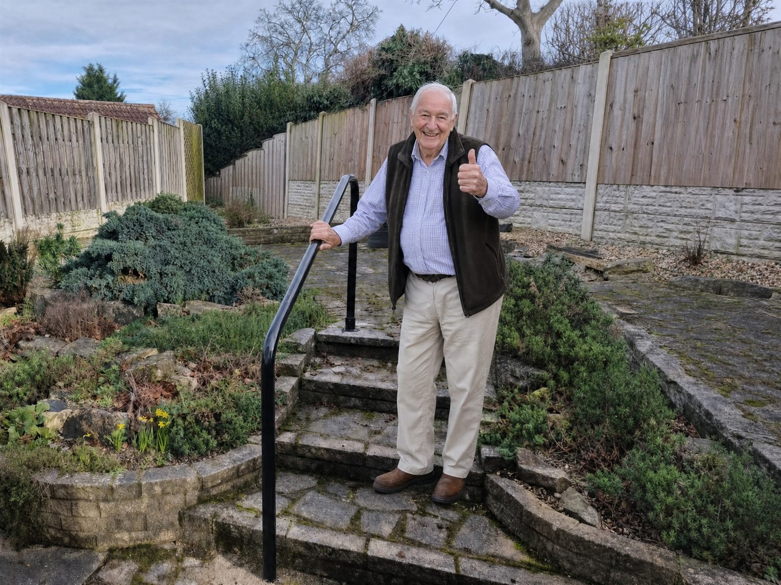 Smiling elderly man using a welded steel handrail on garden steps